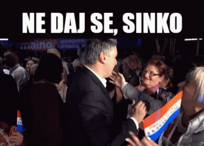 A Man In A Suit Stands In Front Of A Crowd With The Words Ne Daj Se Sinko On The Top GIF