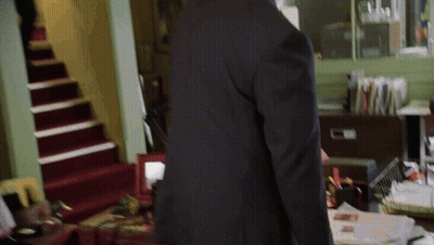 A Man In A Suit Stands In Front Of A Desk With Papers On It GIF