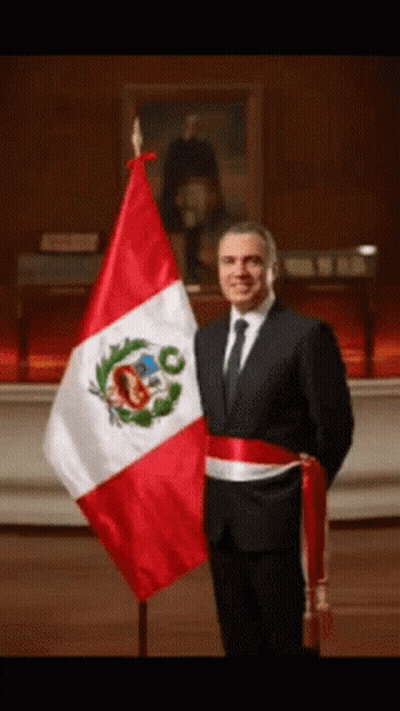 A Man In A Suit Stands In Front Of A Flag GIF