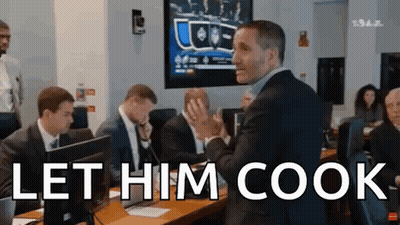 A Man In A Suit Stands In Front Of A Group Of People And Says Let Him Cook .. GIF