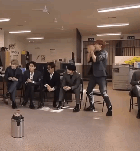 A Man In A Suit Stands In Front Of A Group Of People Sitting In Chairs GIF