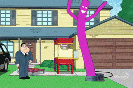 A Man In A Suit Stands In Front Of A House With A Purple Air Dancer GIF