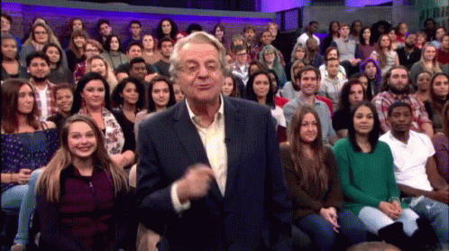 A Man In A Suit Stands In Front Of A Large Crowd GIF