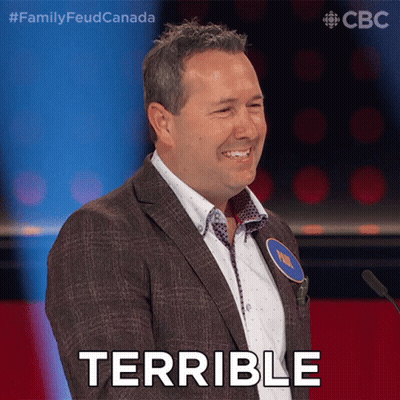 A Man In A Suit Stands In Front Of A Microphone With The Word Terrible On His Face GIF