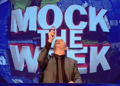 A Man In A Suit Stands In Front Of A Mock The Week Sign GIF