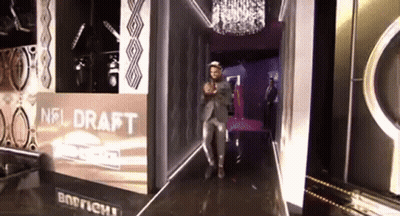A Man In A Suit Stands In Front Of A Nfl Draft Sign GIF