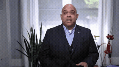 A Man In A Suit Stands In Front Of A Plant GIF