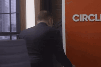 A Man In A Suit Stands In Front Of A Red Sign That Says Circle GIF