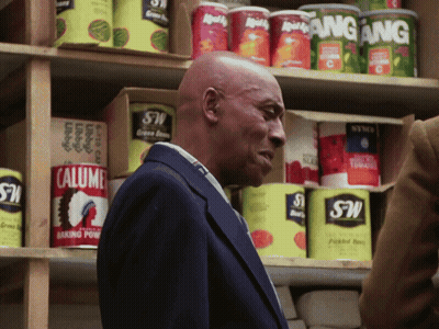 A Man In A Suit Stands In Front Of A Shelf Full Of Cans Including Calumet Baking Powder GIF