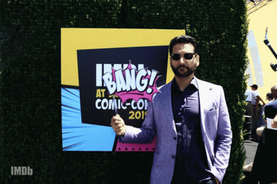 A Man In A Suit Stands In Front Of A Sign That Says " Bang " GIF