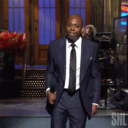 A Man In A Suit Stands In Front Of A Sign That Says Snl GIF