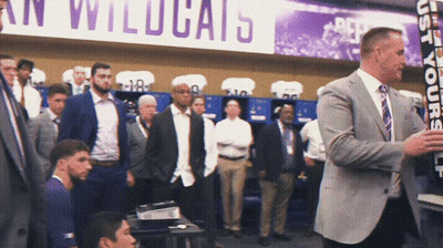 A Man In A Suit Stands In Front Of A Sign That Says " Wildcats " GIF