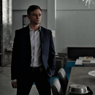 A Man In A Suit Stands In Front Of A Table With His Hands In His Pockets GIF