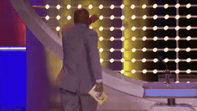 A Man In A Suit Stands In Front Of A Wall Of Lights Holding A Magazine GIF