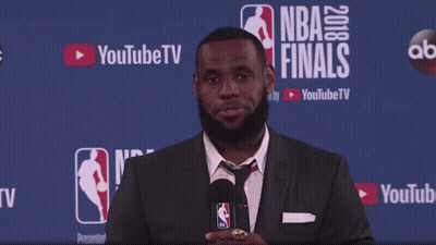 A Man In A Suit Stands In Front Of A Wall That Says Nba Finals GIF