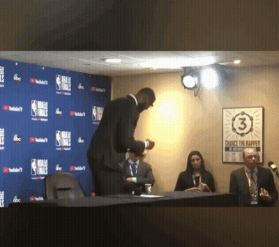 A Man In A Suit Stands In Front Of A Wall That Says Nba Finals On It GIF