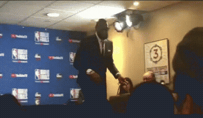 A Man In A Suit Stands In Front Of A Wall With The Number 3 GIF