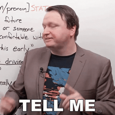 A Man In A Suit Stands In Front Of A White Board And Says Tell Me GIF