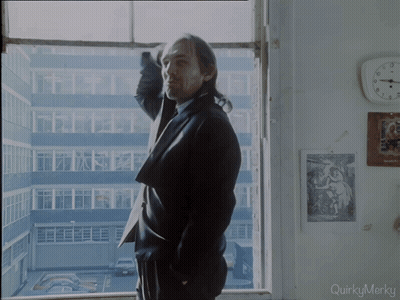 A Man In A Suit Stands In Front Of A Window With Quirkymerky Written On The Bottom GIF