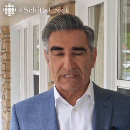 A Man In A Suit Stands In Front Of A Window With #Schitts Creek On The Bottom GIF