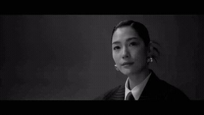 A Man In A Suit Stands In Front Of A Woman Sitting At A Table GIF