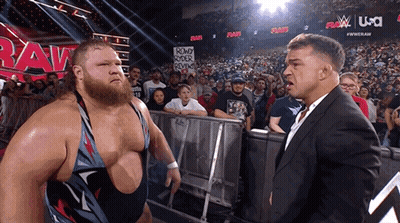 A Man In A Suit Stands Next To A Man In A Wrestling Ring With A Sign That Says Round Rock Reviews GIF