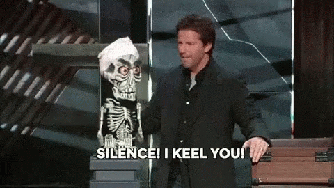 A Man In A Suit Stands Next To A Skeleton Puppet And Says Silence I Keel You GIF