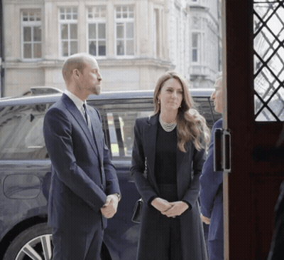 A Man In A Suit Stands Next To A Woman In A Black Dress GIF