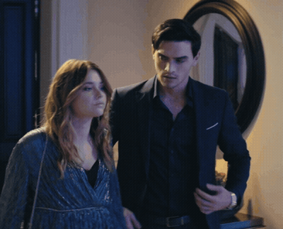 A Man In A Suit Stands Next To A Woman In A Blue Dress GIF