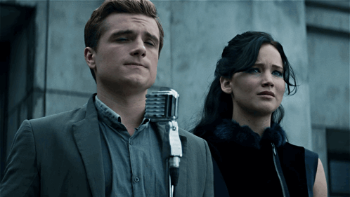 A Man In A Suit Stands Next To A Woman In A Fur Coat GIF