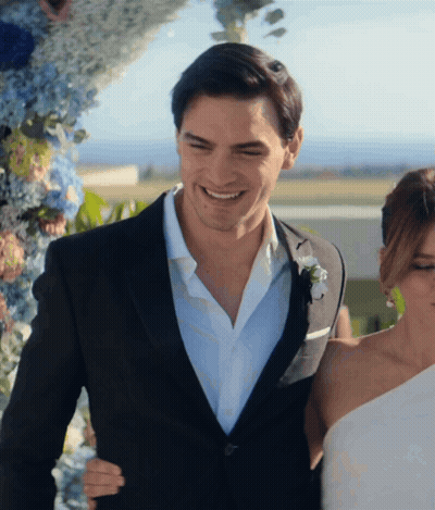 A Man In A Suit Stands Next To A Woman In A Wedding Dress GIF