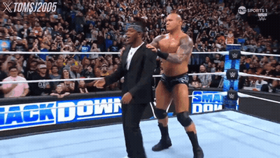 A Man In A Suit Stands Next To A Wrestler In A Wrestling Ring That Says Back Down GIF