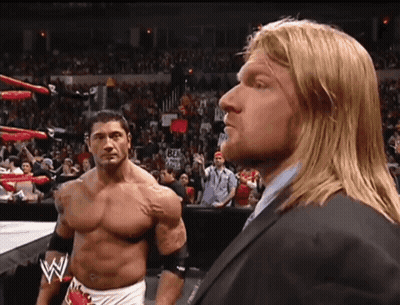 A Man In A Suit Stands Next To Another Man In A Wrestling Ring GIF