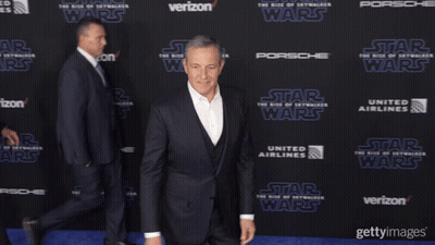 A Man In A Suit Stands On A Blue Carpet With The Word Star Wars On It GIF