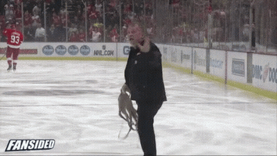 A Man In A Suit Stands On A Hockey Rink In Front Of An Nhl.com Sign GIF