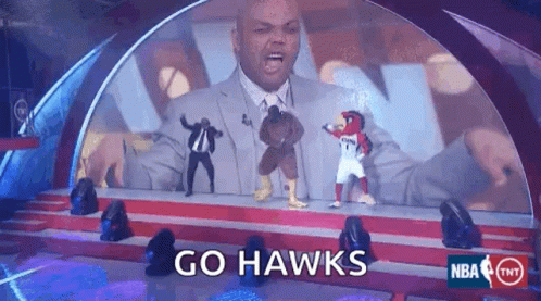 A Man In A Suit Stands On A Stage With A Hawks Mascot GIF
