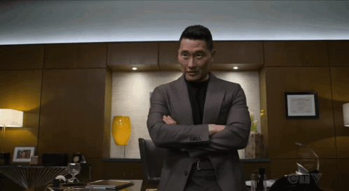 A Man In A Suit Stands With His Arms Crossed In Front Of A Sign That Says Ctv On It GIF