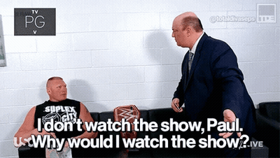 A Man In A Suit Talks To A Man In A Black Shirt That Says Suplex City GIF