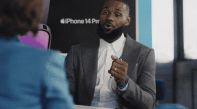 A Man In A Suit Talks To A Woman In Front Of An Iphone 14 Pro GIF