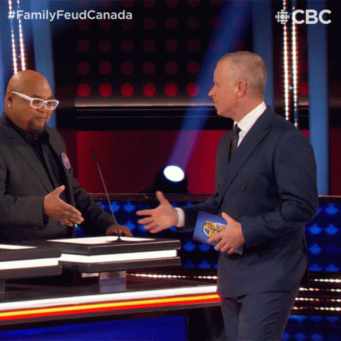 A Man In A Suit Talks To Another Man On A Stage With A Cbs Logo In The Background GIF