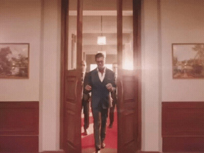 A Man In A Suit Walks Through A Doorway GIF