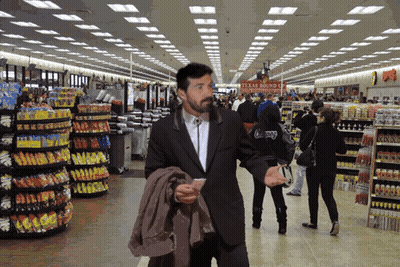 A Man In A Suit Walks Through A Grocery Store With A Sign That Says Texas Roundup GIF