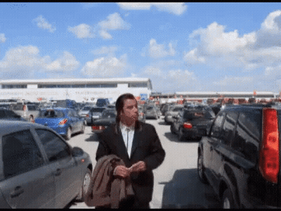 A Man In A Suit Walks Through A Parking Lot GIF
