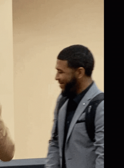 A Man In A Suit With A Backpack On His Back Is Smiling GIF