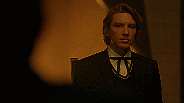 A Man In A Suit With A Bow Tie Is Standing In A Dark Room GIF