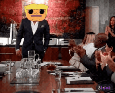 A Man In A Suit With A Cartoon Face On His Head Stands In Front Of A Group Of People Clapping GIF