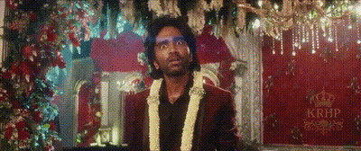 A Man In A Suit With A Garland Around His Neck Is Standing In Front Of A Red Curtain . GIF