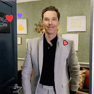 A Man In A Suit With A Heart On His Jacket Is Standing In A Doorway . GIF