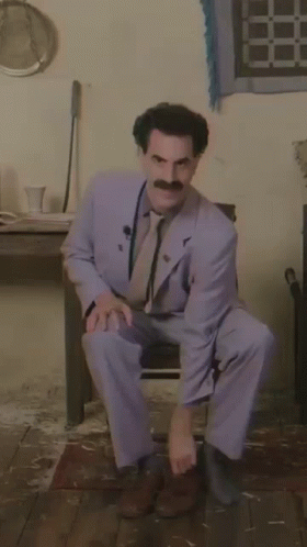 A Man In A Suit With A Mustache Is Squatting Down GIF
