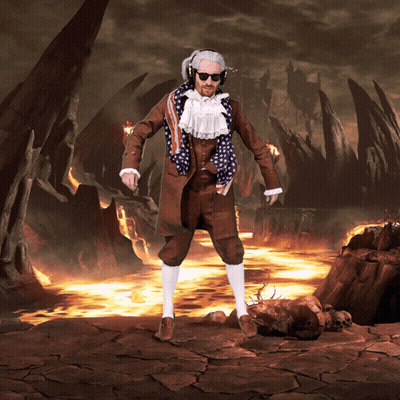 A Man In A Suit With An American Flag Scarf Around His Neck Stands In Front Of A Volcano GIF